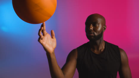 Studioporträtaufnahme-Eines-Männlichen-Basketballspielers,-Der-Vor-Rosa-Und-Blau-Beleuchtetem-Hintergrund-Einen-Ball-Auf-Dem-Finger-Dreht-2